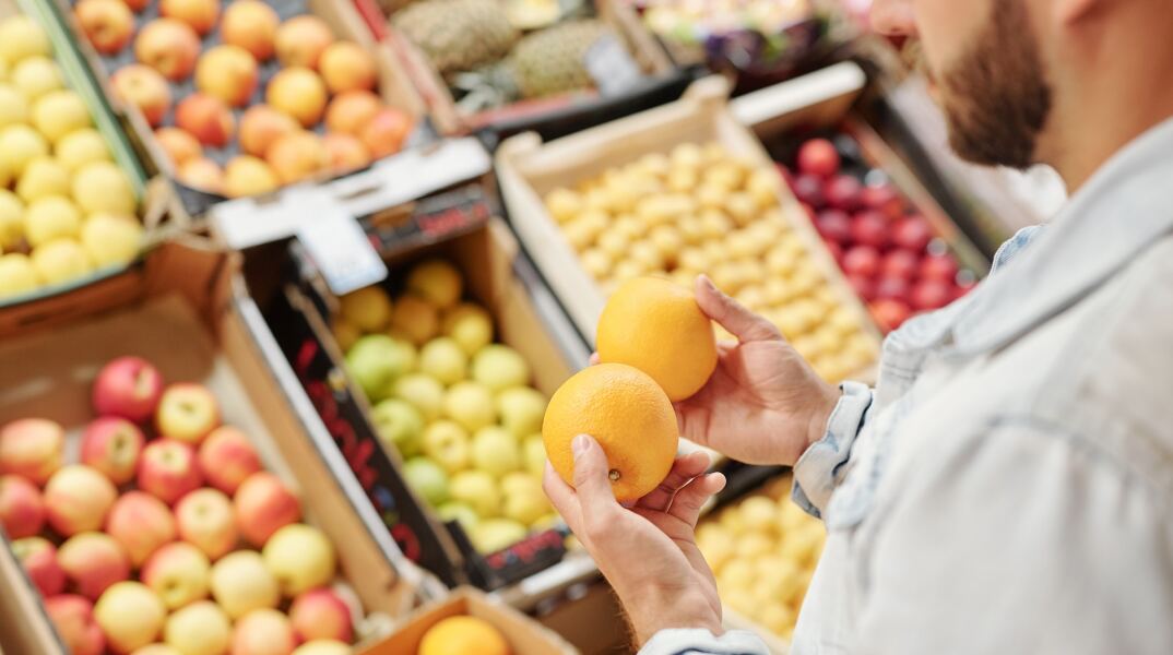 Άνδρας κρατά πορτοκάλια μπροστά από τον τομέα με φρούτα και λαχανικά σε σούπερ μάρκετ