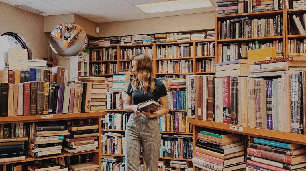Νεαρή γυναίκα σε βιβλιοπωλείο εξετάζει προσεκτικά τα βιβλία που επιθυμεί να αγοράσει