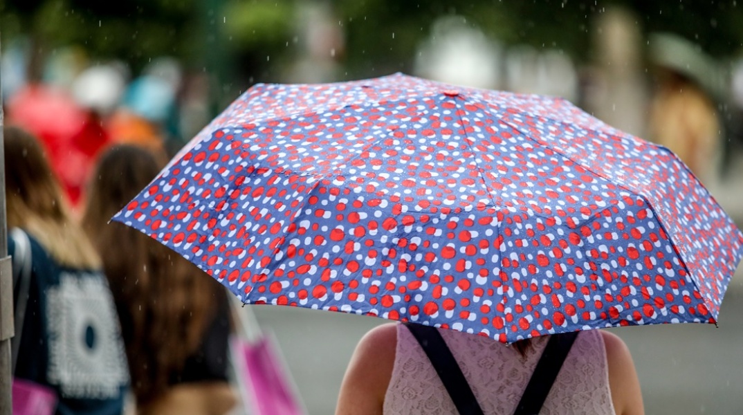 Γυναίκα κρατά ομπρέλα σε καλοκαιρινή βροχή