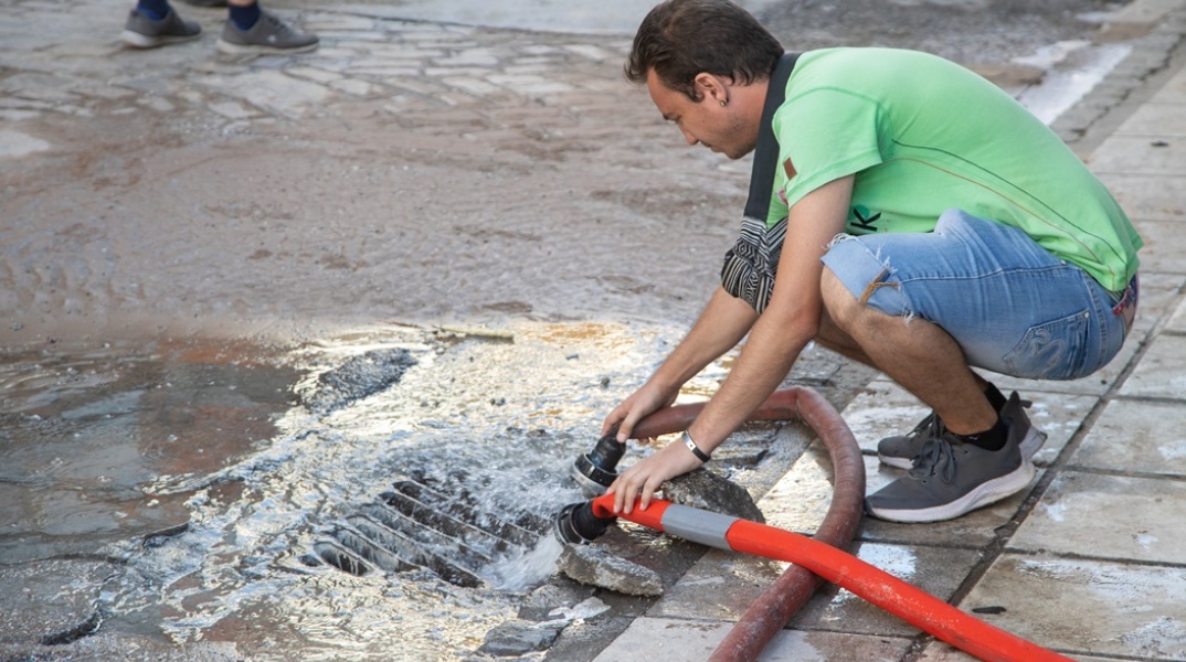 Άνδρας πάνω από φρεάτιο στο οποίο πέφτουν τα νερά μετά τη θραύση αγωγού στη Θεσσαλονίκη