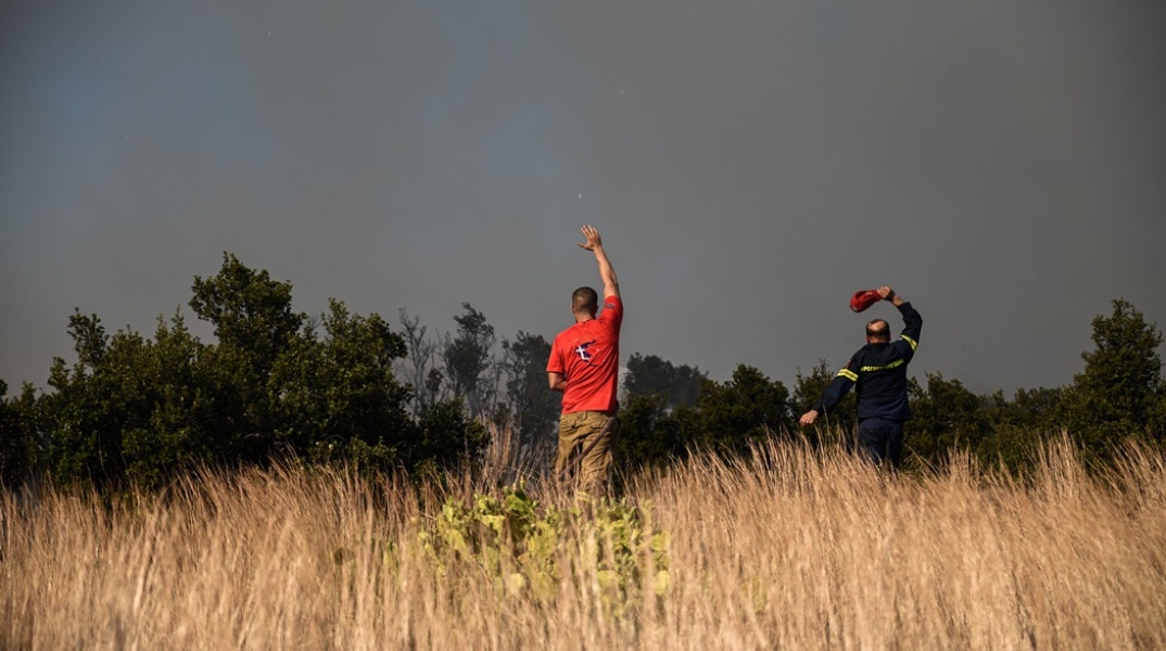 Πυροσβέστης και εθελοντής μακριά από το πύρινο μέτωπο επιτηρούν φωτιά που καίει χαμηλή βλάστηση