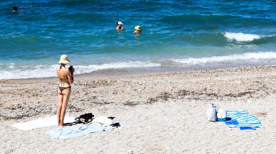 Γυναίκα σε παραλία όρθια κοντά στην απλωμένη πετσέτα της - παραλία με λίγο κυματάκι