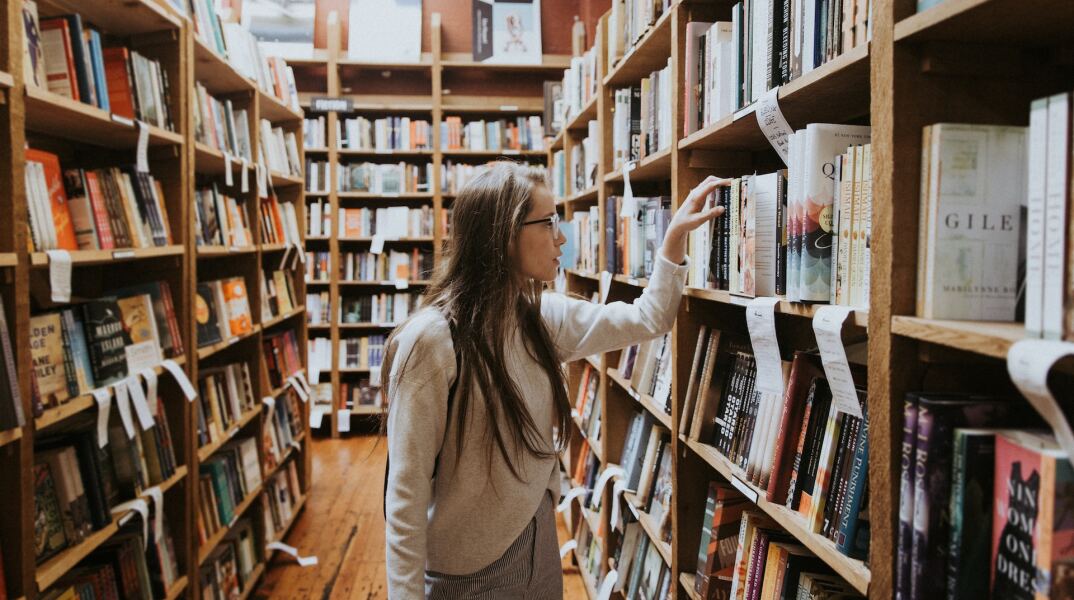 Γυναίκα κοντά σε ράφια βιβλιοπωλείου κοιτά βιβλία