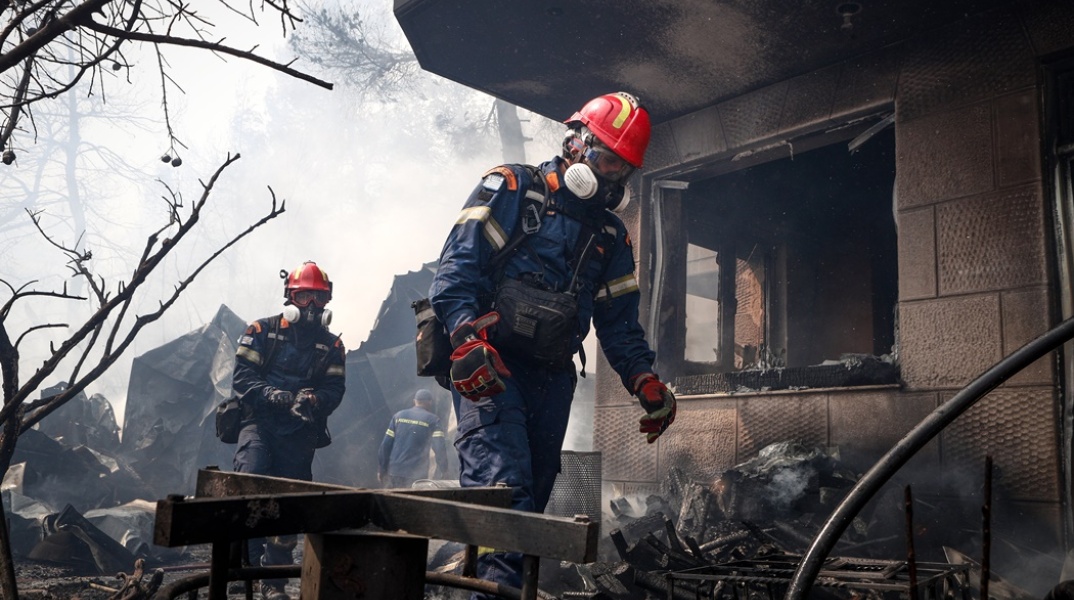 Πυροσβέστες περπατούν δίπλα σε καμένα σπίτια