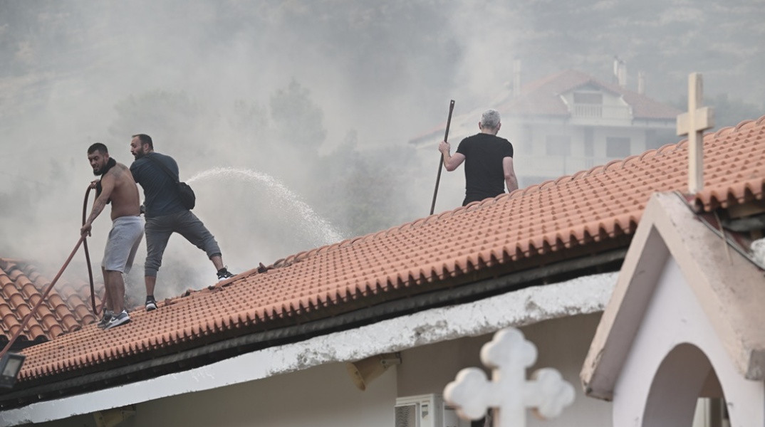 Εθελοντές με τη μάνικα νερού επιχειρούν για την κατάσβεση της πυρκαγιάς