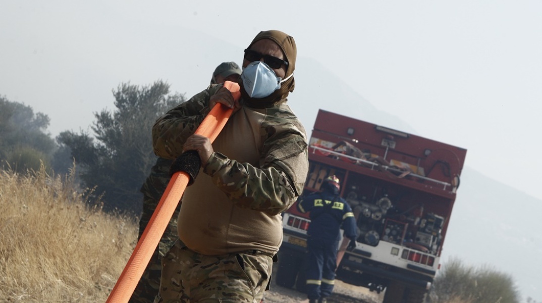 Πυροσβέστης και εθελοντής κουβαλούν τη μάνικα από το πυροσβεστικό όχημα για την κατάσβεση φωτιάς