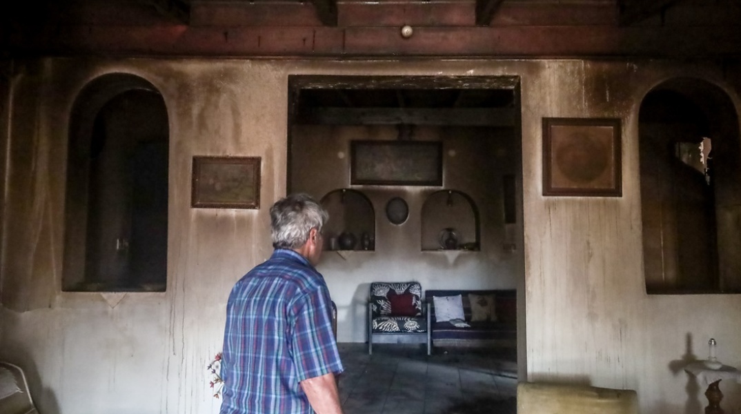 Πολίτης μπαίνει στο σπίτι του που έχει υποστεί καταστροφές από τις φλόγες στην Αγία Παρασκευή