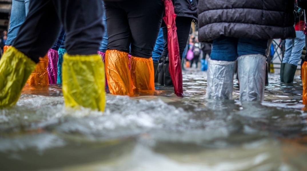 Πολίτες με προστατευτικά αδιάβροχα στα πόδια σε πλημμυρισμένο δρόμο