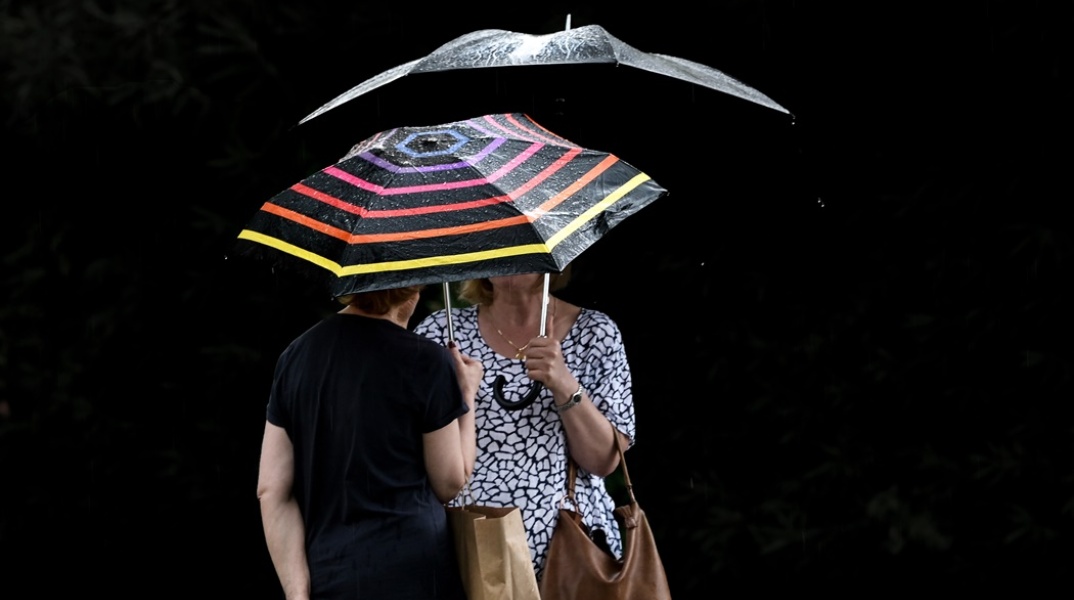 Γυναίκες κρατούν ομπρέλα για να προστατευτούν από τη βροχή και μιλάνε