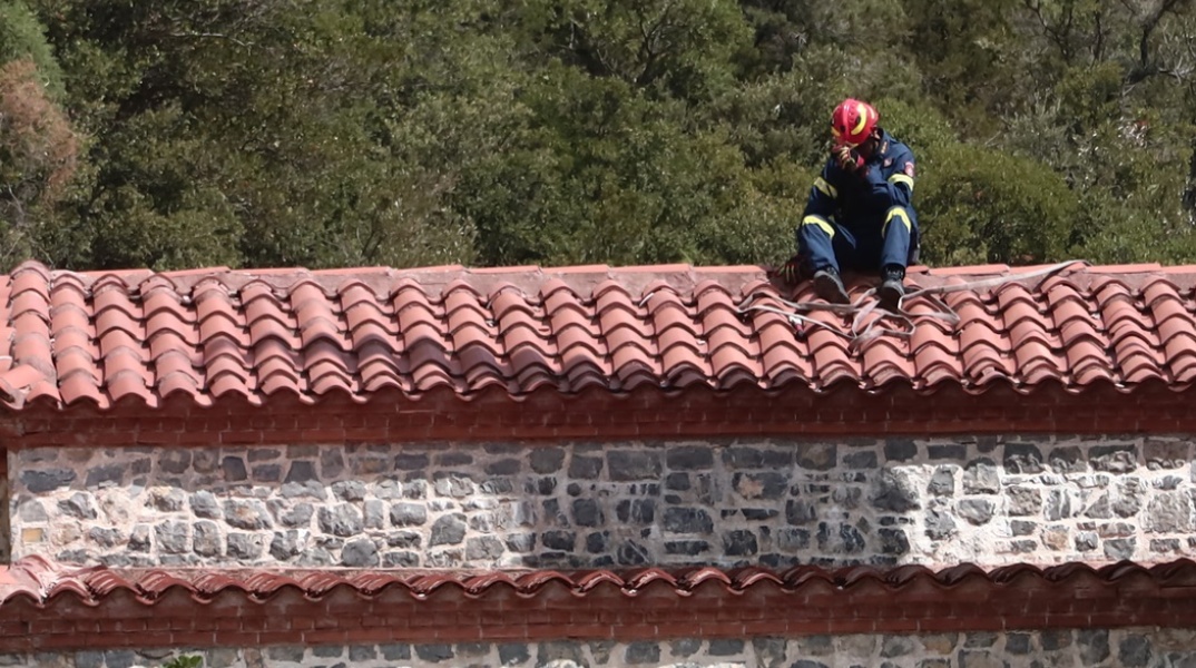 Πυροσβέστης σε σκεπή σπιτιού φανερά εξαντλημένος από την επιχείρηση κατάσβεσης φωτιάς