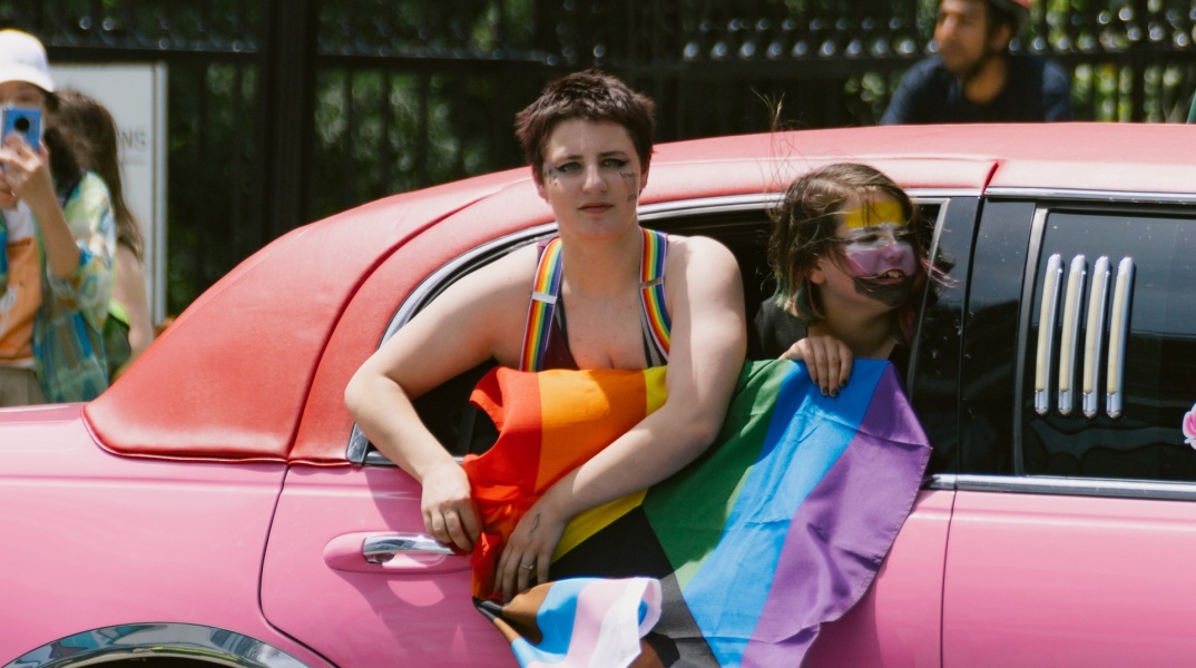 Άτομο μέσα σε αυτοκίνητο κρατά σημαία της ΛΟΑΤΚΙ+ κοινότητας