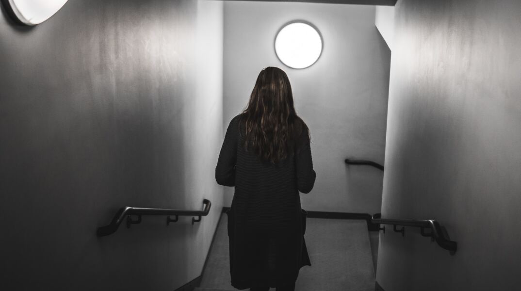 Γυναίκα γυρισμένη πλάτη σε σκοτεινό διάδρομο - Εικόνα που παραπέμπει σε κακοποίηση και μυστήριο