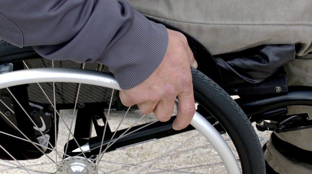 Άτομο σε αναπηρικό αμαξίδιο πιάνει το σύστημα μετακίνησης δίπλα από τις ρόδες