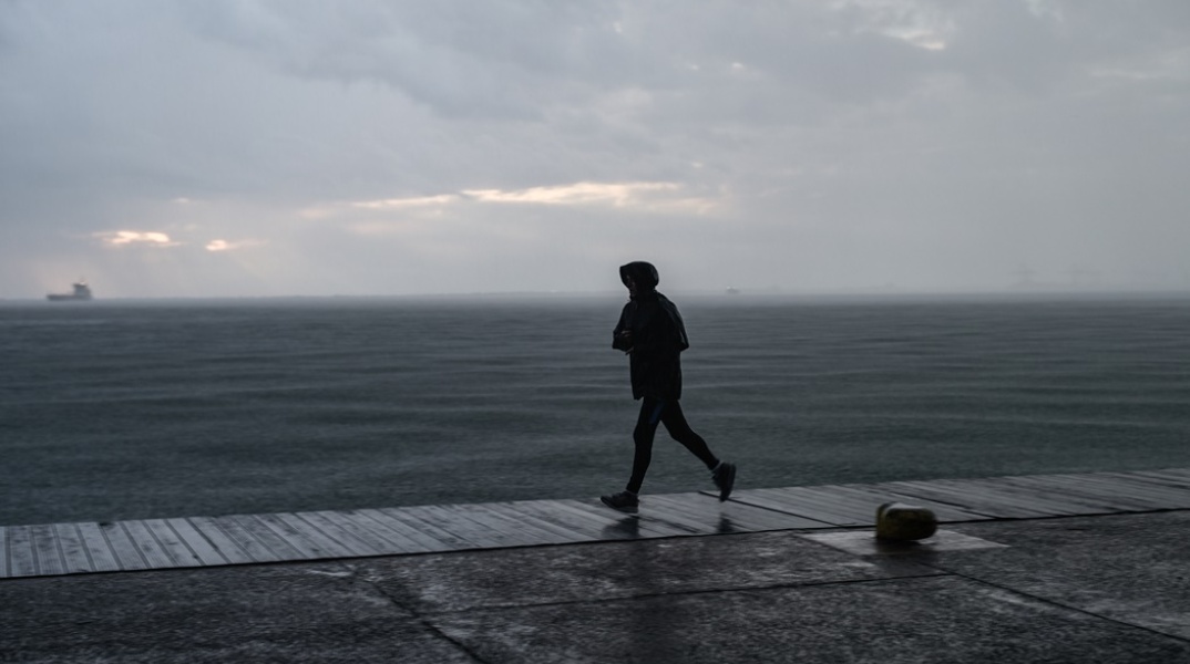 Πολίτης με αδιάβροχο τρέχει στην παραλία της Θεσσαλονίκης