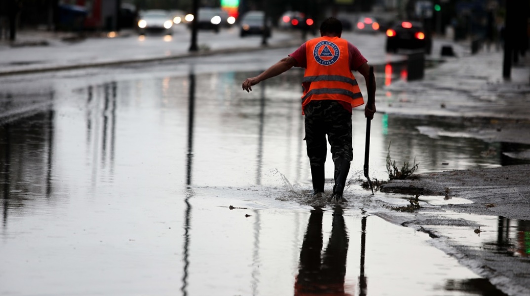 Πλημμυρισμένο σημείο της οδού Πειραιώς και άτομο που επιχειρεί να ανοίξει φρεάτια
