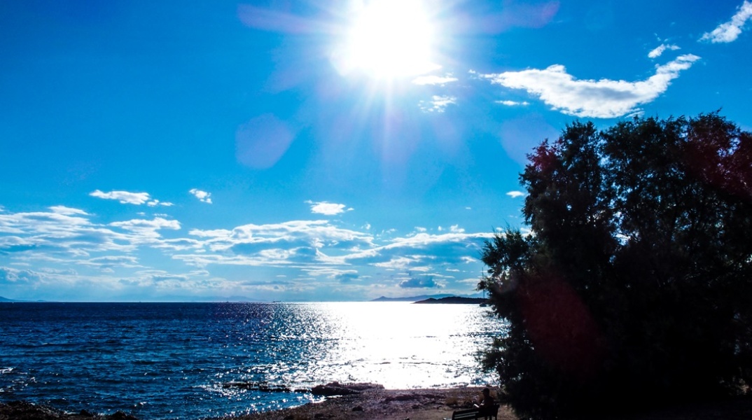 Ήλιος λαμπερός και λίγα σύννεφα πάνω από παραλία