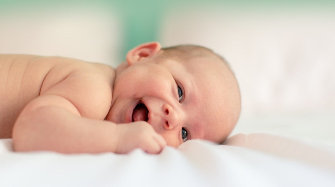 Μωρό που χαμογελά ξαπλωμένο σε λευκό σεντονάκι