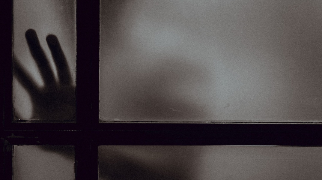 Σκοτεινή φωτογραφία με χέρι ατόμου πίσω από κλειστή πόρτα