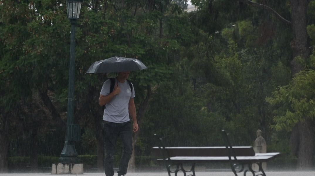 Νεαρός περπατά εν μέσω καταιγίδας κρατώντας ομπρέλα 
