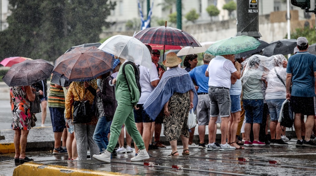 Πολίτες στο κέντρο της Αθήνας προσπαθούν να προστατευτούν από καταιγίδα