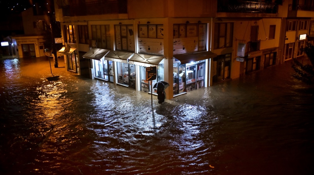 Άνδρας στον Βόλο περπατά με ομπρέλα σε πλημμυρισμένο δρόμο ενώ το νερό του φτάνει μέχρι το γόνατο