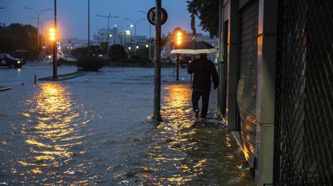 Άνδρας περπατά σε πλημμυρισμένο δρόμο στον Βόλο