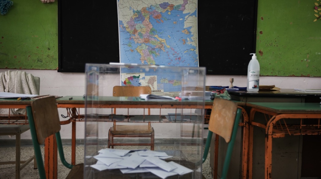 Κάλπη με ψηφοδέλτια μπροστά από χάρτη της Ελλάδας σε εκλογικό τμήμα - σχολική αίθουσα