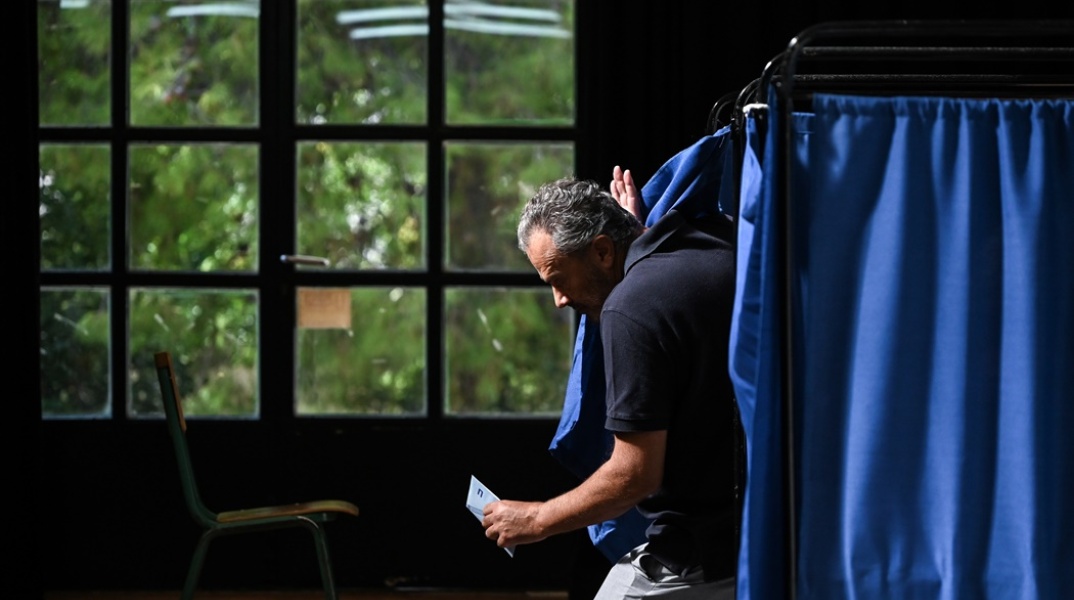 Ψηφοφόρος βγαίνει από το παραβάν κρατώντας στα χέρια του το ψηφοδέλτιο