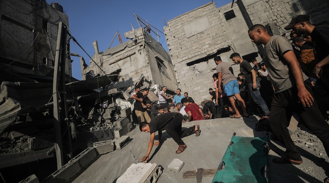 Πολίτες δίπλα σε κατεστραμμένο κτίριο στη Γάζα