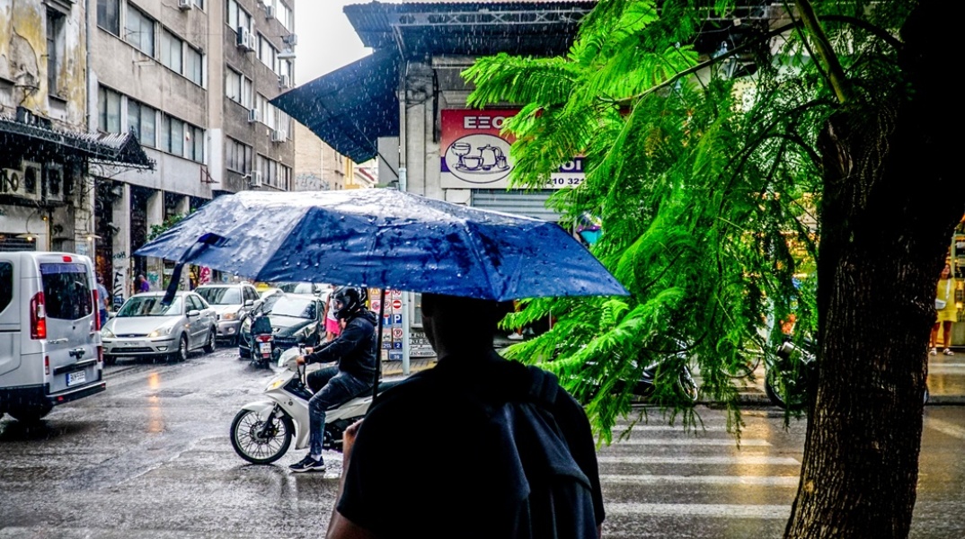 Άνδρας με ομπρέλα περπατά υπό βροχή σε δρόμο της Αθήνας