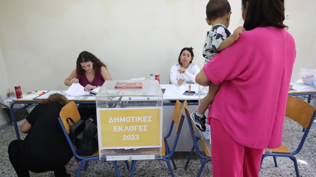 Γυναίκα κρατά το παιδί της στην αγκαλιά και προσέρχεται στην κάλπη για τις Αυτοδιοικητικές Εκλογές 2023