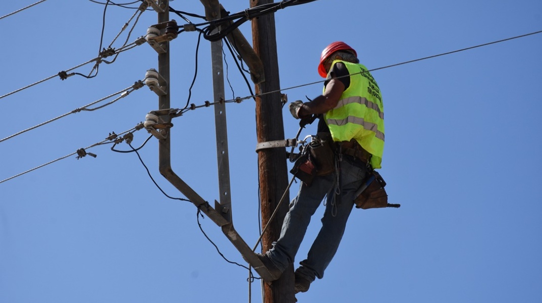 Τεχνίτης σκαρφαλωμένος σε κολώνα της ΔΕΗ φορά τα προστατευτικά ρούχα