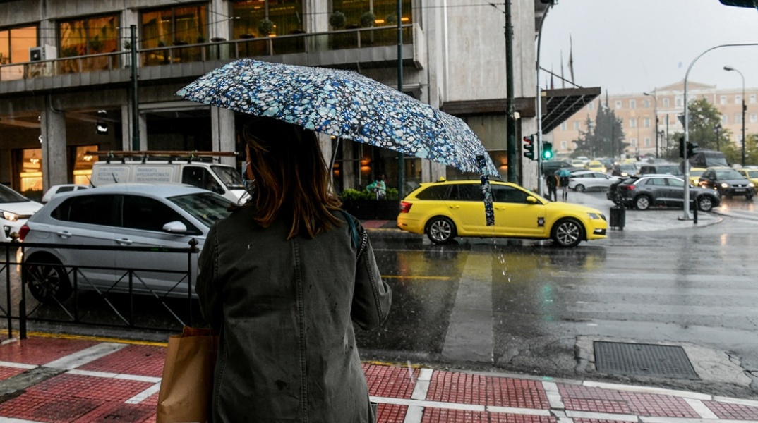 Γυναίκα με ομπρέλα σε δρόμο της Αθήνας περιμένει το φανάρι για να διασχίσει δρόμο