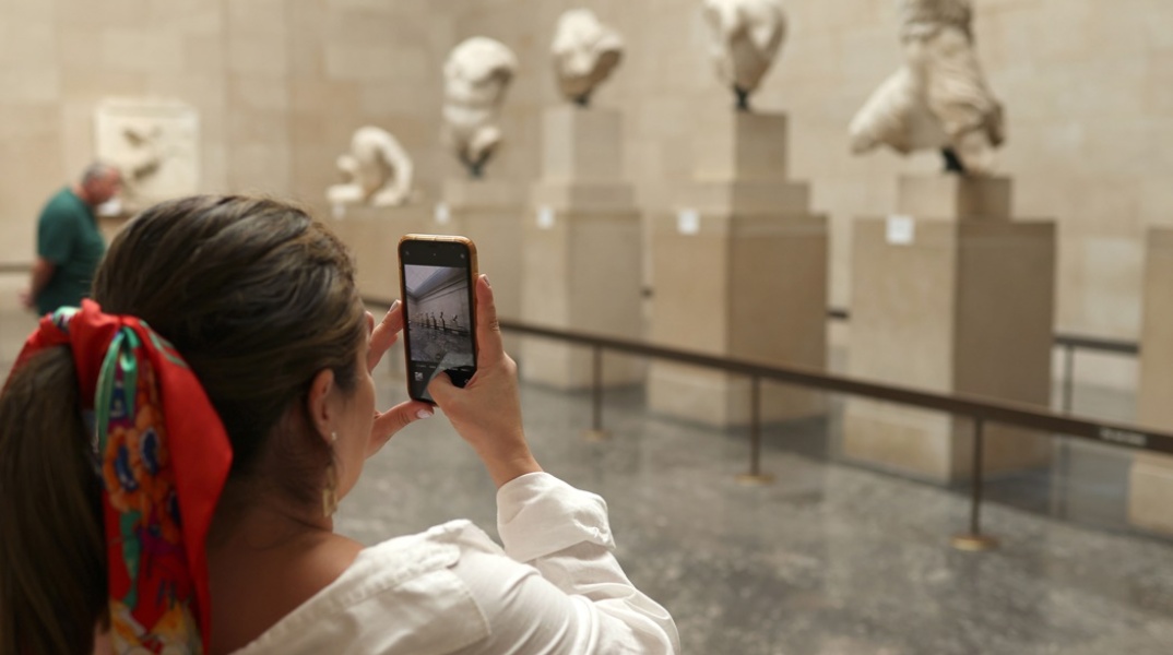 Τεκμήρια στο Βρετανικό Μουσείο και γυναίκα στα αριστερά της οθόνης που με το κινητό της τα φωτογραφίζει