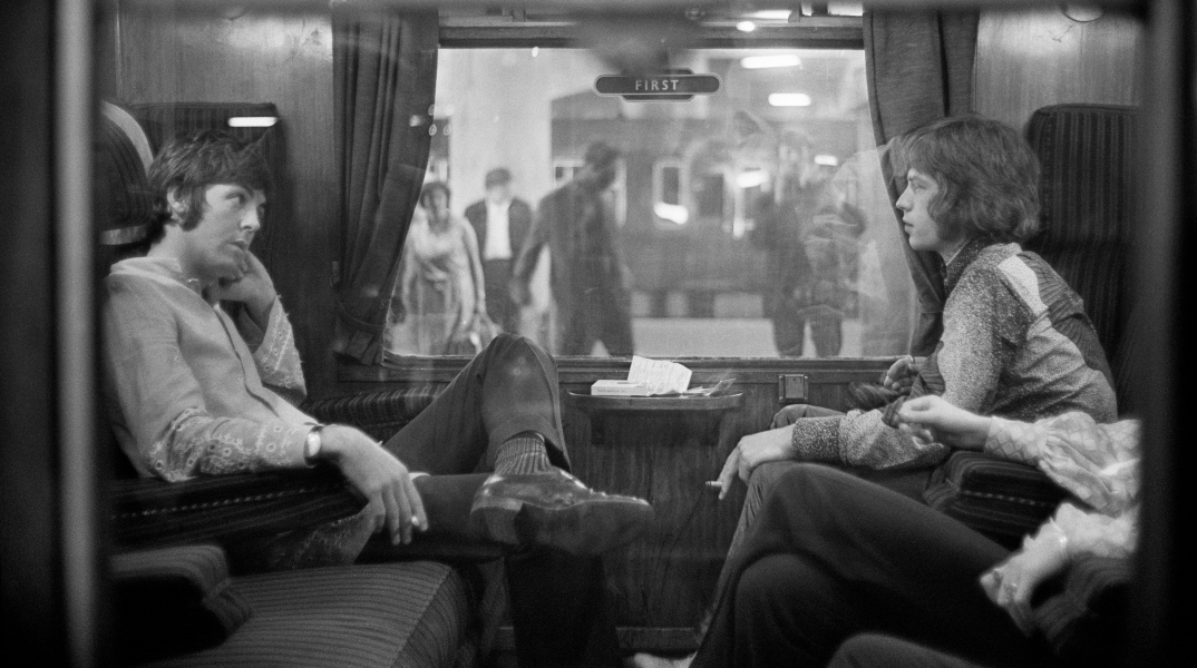 Ο Paul McCartney των Beatles και ο Mick Jagger των Rolling Stones κάθονται ο ένας απέναντι από τον άλλο σε ένα τρένο στο σταθμό Euston, περιμένοντας την αναχώρηση για το Bangor,