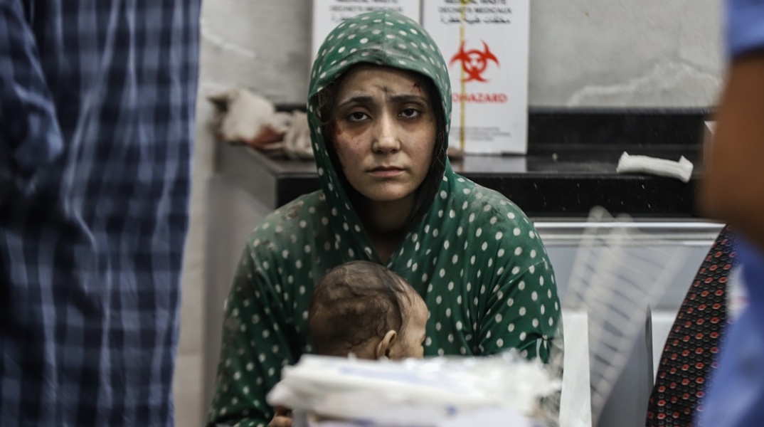 Μητέρα με την απόγνωση ζωγραφισμένη στο πρόσωπό της κοιτά τον φακό και κρατά στην αγκαλιά της το μωρό της μέσα στο νοσοκομείο Αλ Σίφα στη Γάζα