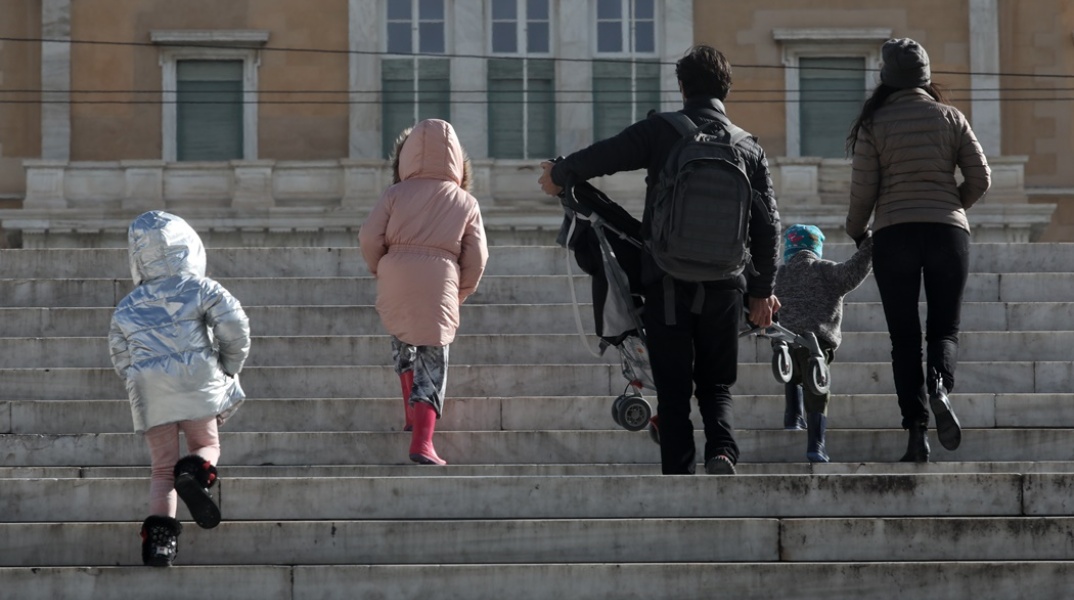 Πολίτες με παιδιά και με χοντρά ρούχα και σκουφιά για το κρύο ανεβαίνουν τα σκαλιά στην πλατεία Συντάγματος
