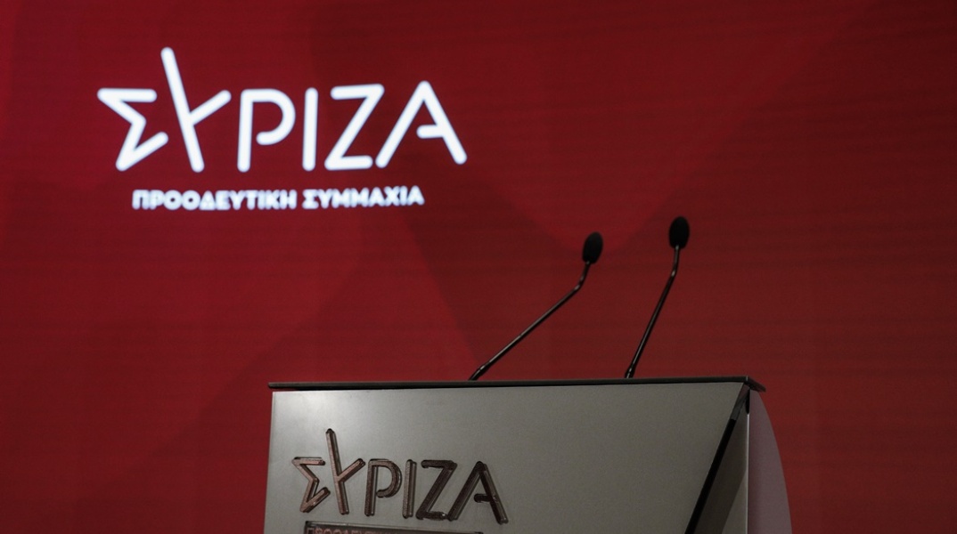 Το λογότυπο του ΣΥΡΙΖΑ με πόντιουμ και τοίχο με κόκκινο φόντο