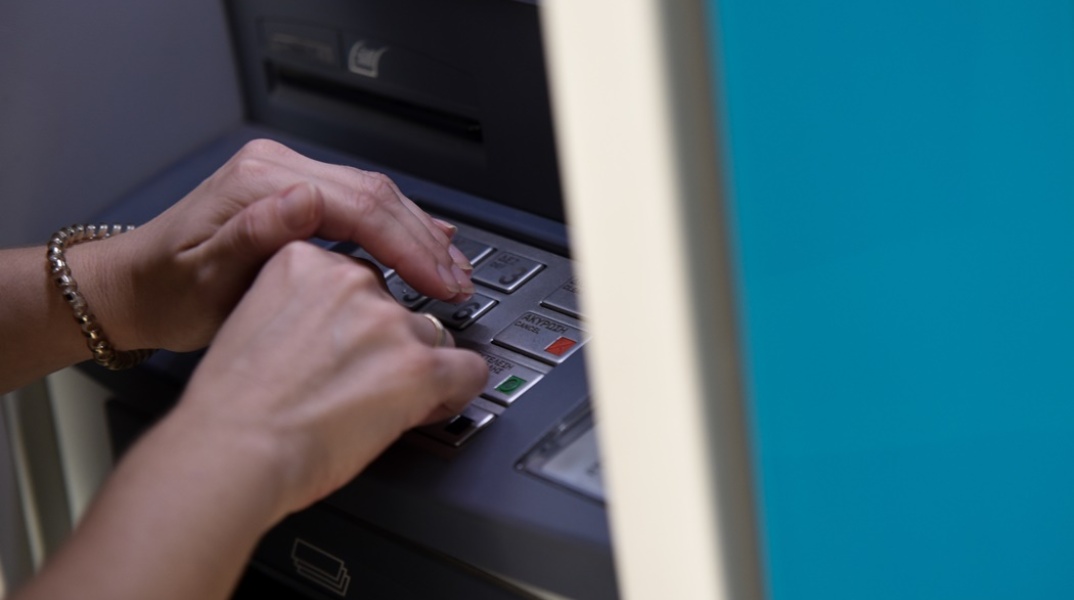 Άτομο μπροστά σε ΑΤΜ πληκτρολογεί τον κωδικό της κάρτας του