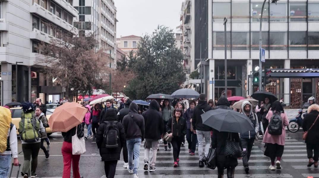 Πολίτες στο Σύνταγμα κρατούν ομπρέλα και περπατούν στον δρόμο υπό βροχή