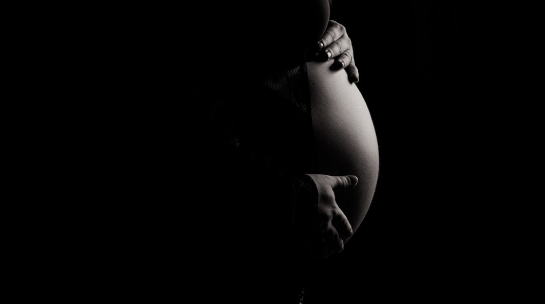 Κοιλία εγκυμονούσας γυναίκας που φωτίζεται ενώ γύρω γύρω υπάρχει σκοτάδι