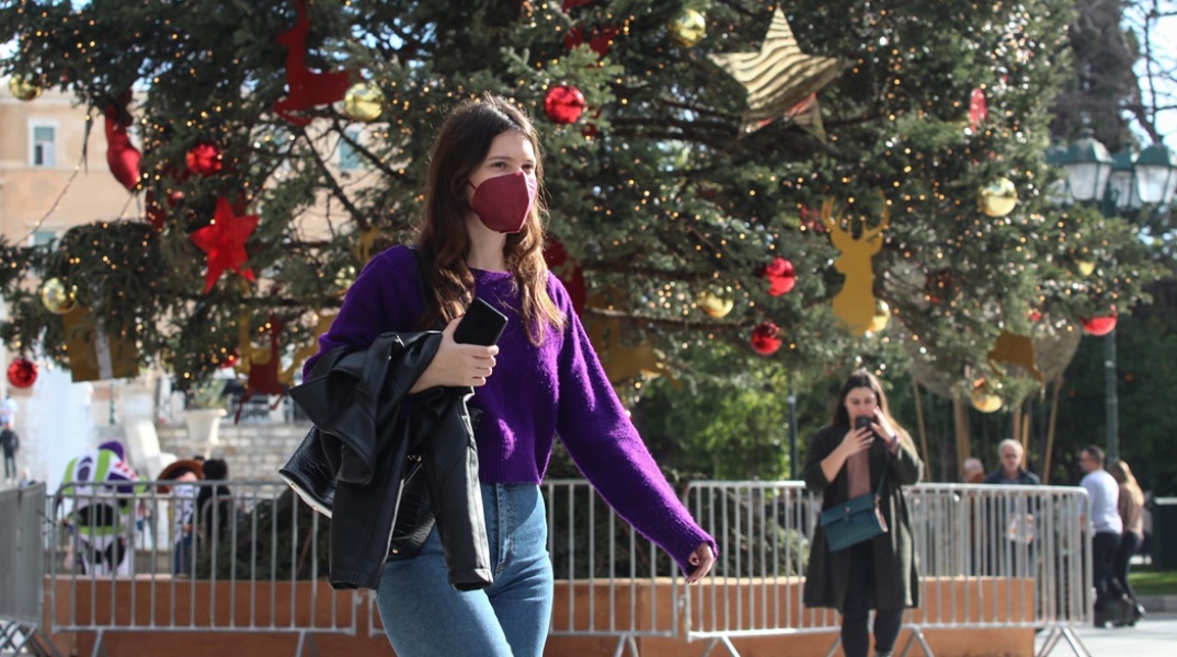 Κοπέλα με μάσκα προστασίας από τον κορωνοϊό μπροστά από το χριστουγεννιάτικο δέντρο στο Σύνταγμα