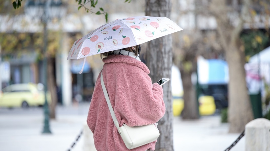 Γυναίκα με χοντρό παλτό για το κρύο, ομπρέλα και το κινητό ανά χείρας