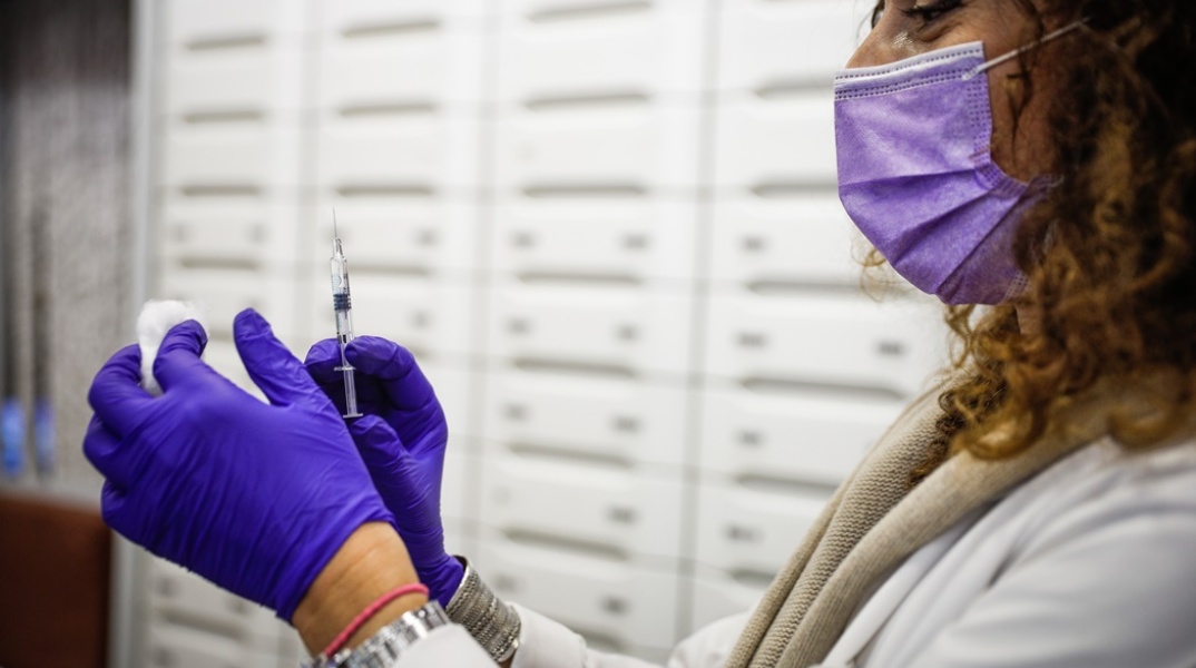 Γυναίκα κρατά εμβόλιο και βαμβάκι στα χέρια της