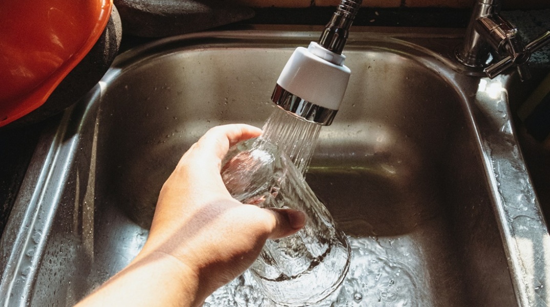 Χέρι που κρατά ποτήρι κάτω από βρύση ενώ ρέει νερό