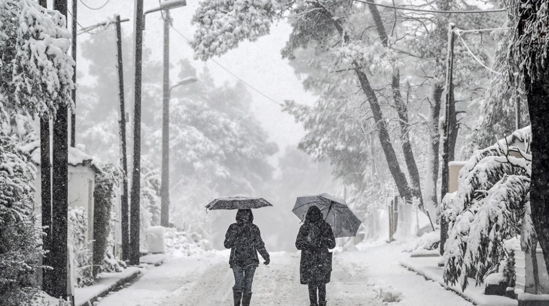 Πολίτες με ανοιχτές τις ομπρέλες τους περπατούν στο χιονισμένο τοπίο