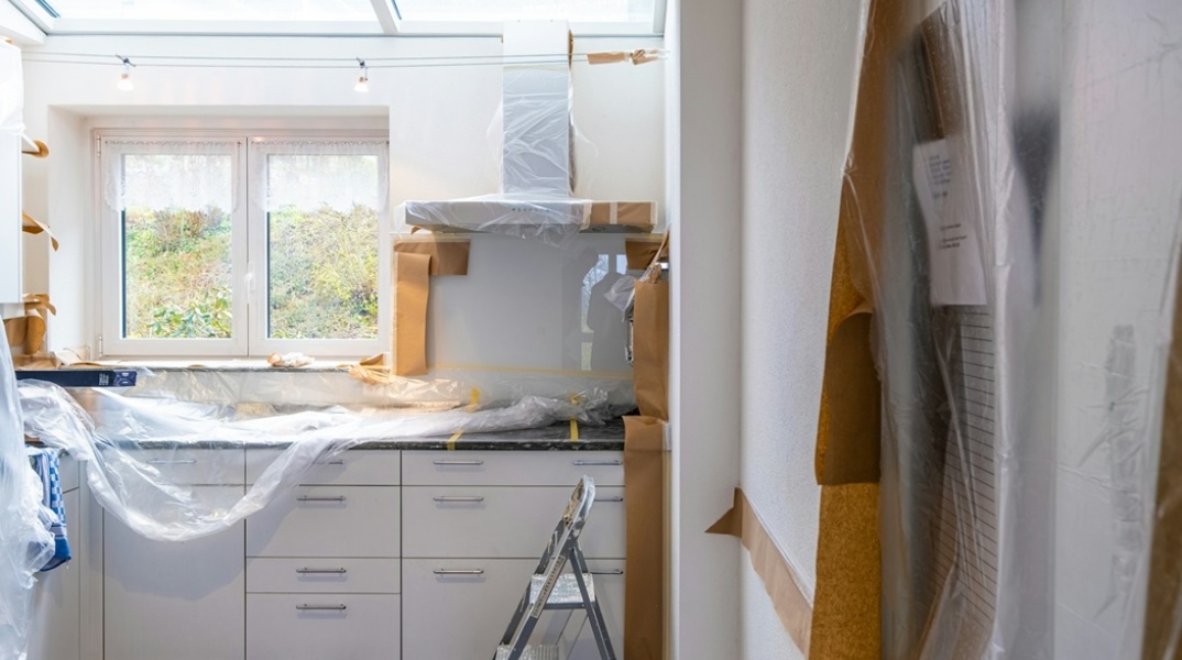Ανακαινισμένη κουζίνα σπιτιού με έπιπλα και συσκευές ακόμα στα προστατευτικά τους