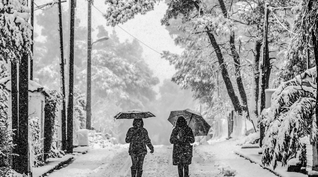 Γυναίκες με ομπρέλες περπατούν σε χιονισμένο τοπίο