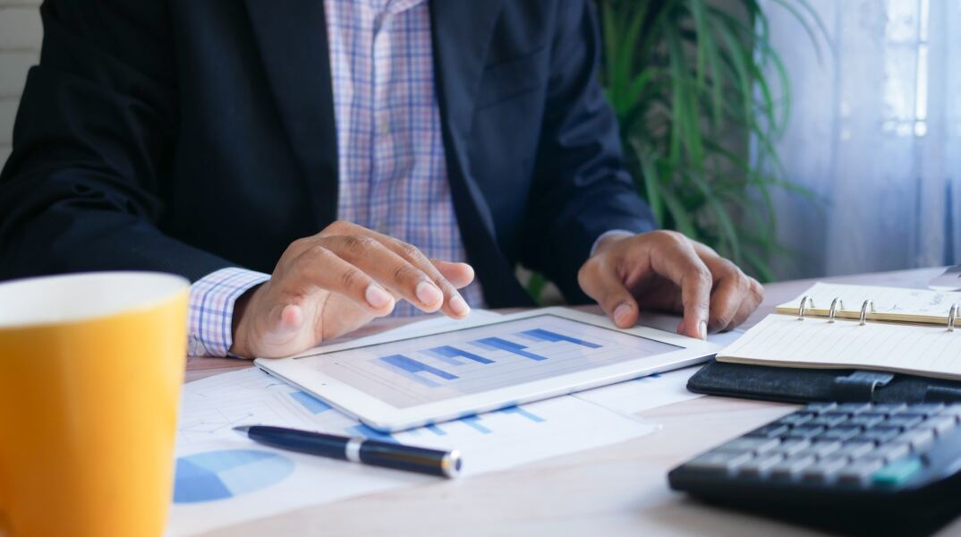 Άτομο με κουστούμι μπροστά από τάμπλετ με μπάρες απεικόνισης στατιστικών