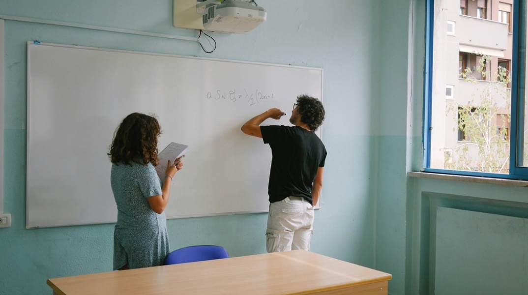 Μαθήτρια και καθηγητής σε τάξη γράφουν στον πίνακα